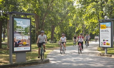 Diverse people cycling in a sunny park with 'Salud en Bicicleta' on a poster