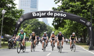 Cyclists riding in an urban park with 'Bajar de peso' park banner